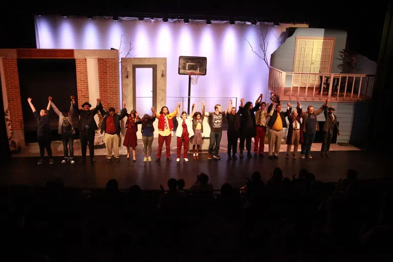 actors lined up on stage interlinking hands for end of show bow