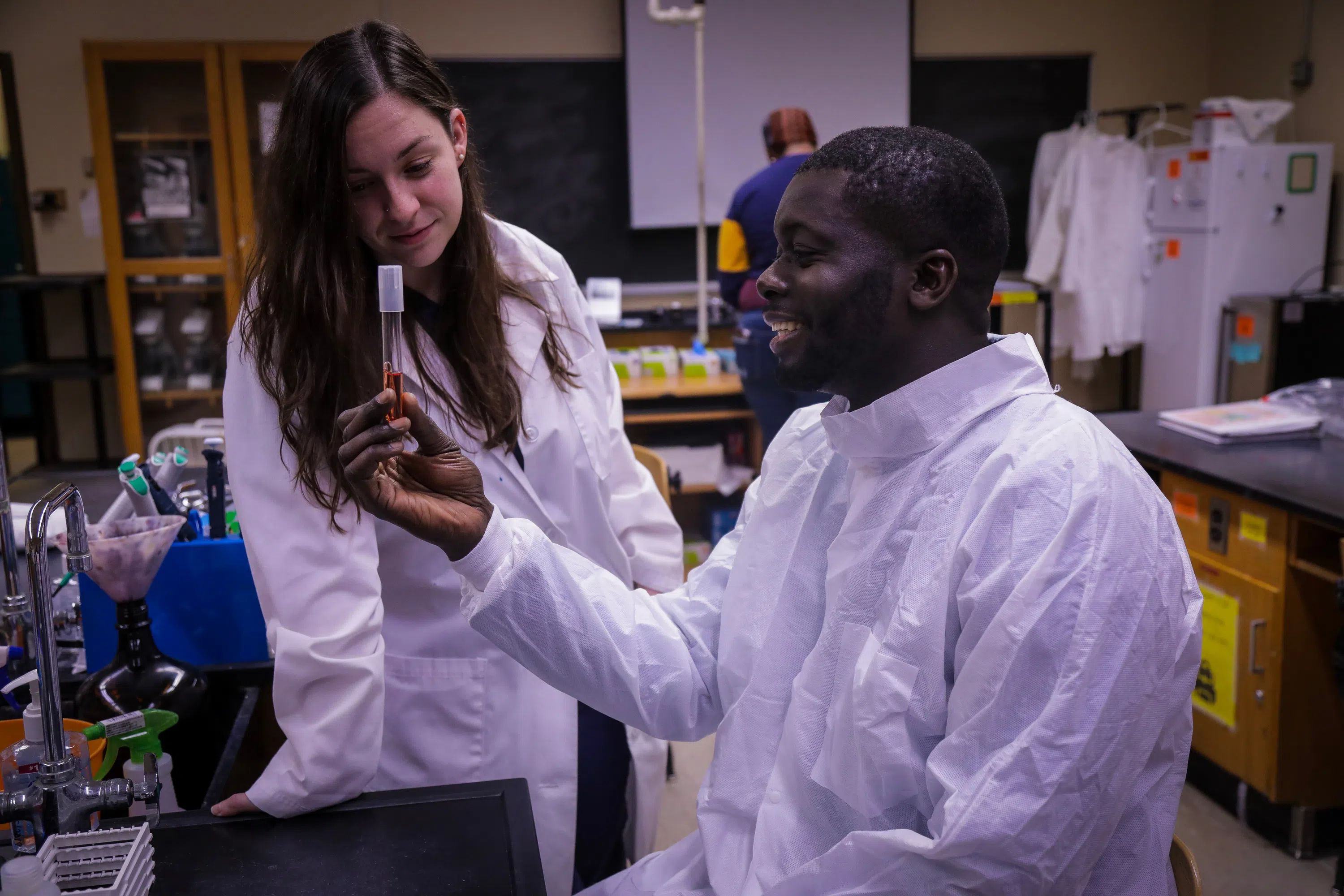 2 students in a biology class looking at vile of orange liquid