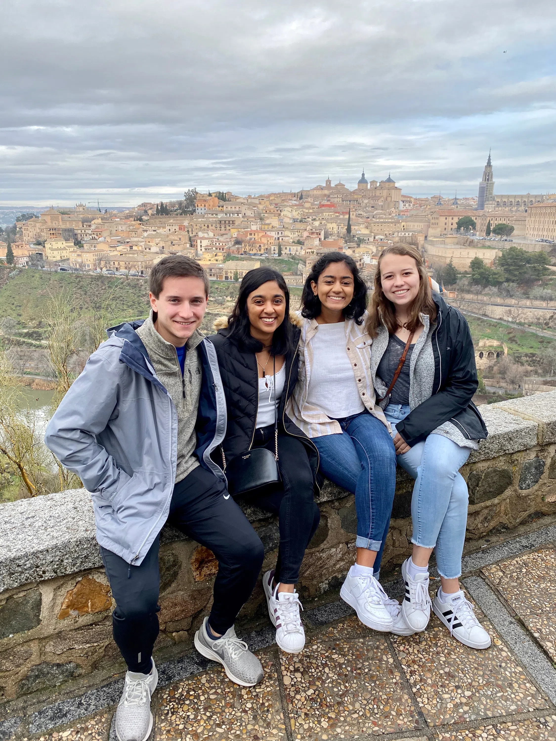 Four students sit on a ledge, which is overlooking an architectural scene in Toledo, Spain.