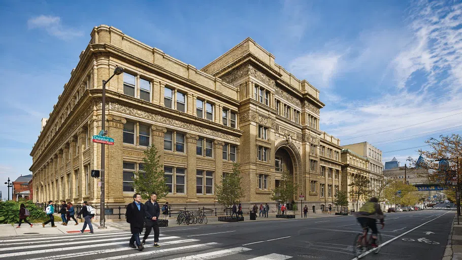 Exterior of historic Main Building and people crossing the street in front of it.