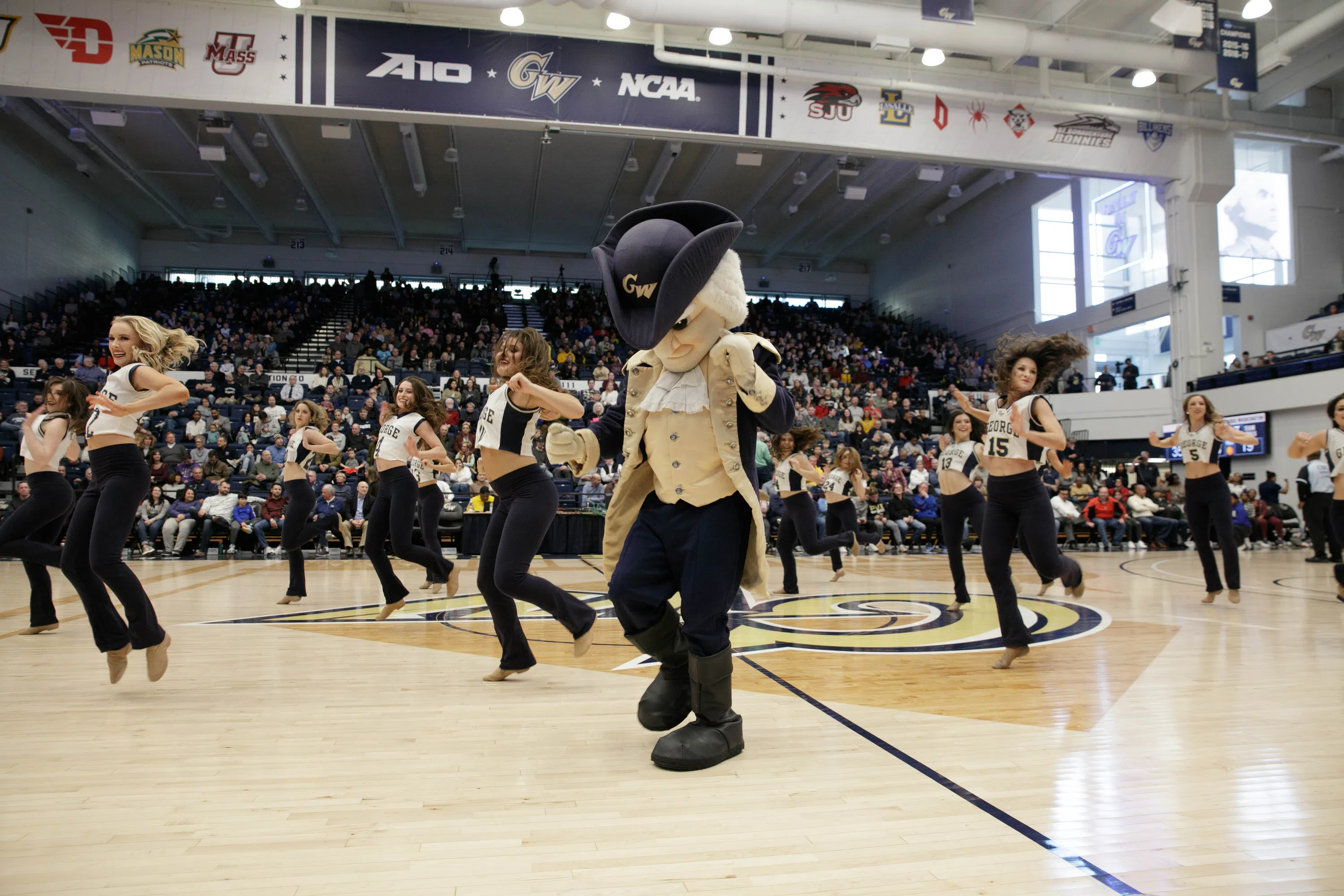 GW mascot and dancers dancing on the basketball court