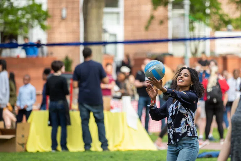 A student plays volleyball in the foreground while others enjoy games in the background