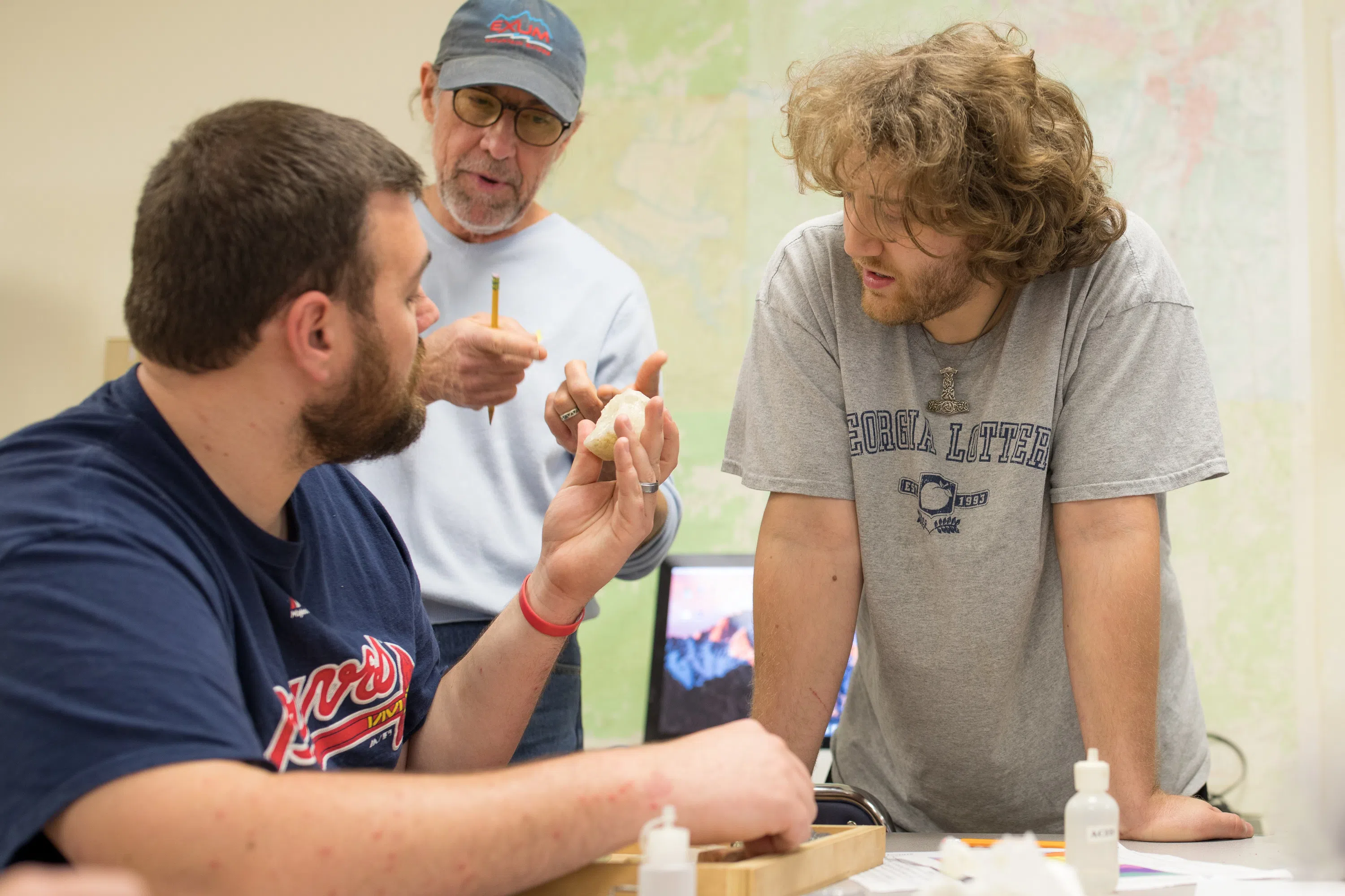 Two student examine a white rock with their professor 