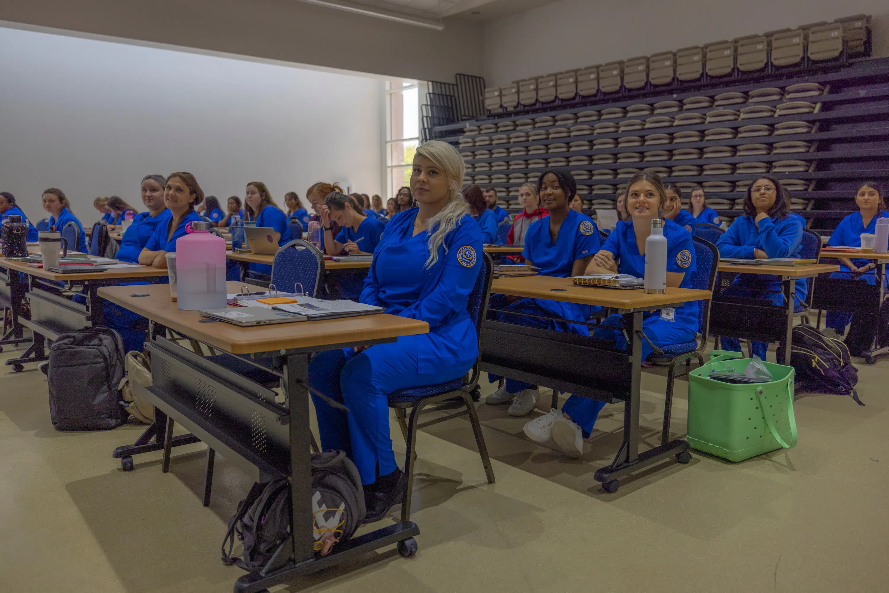 Nursing students sit at rows of tables in the auditorium