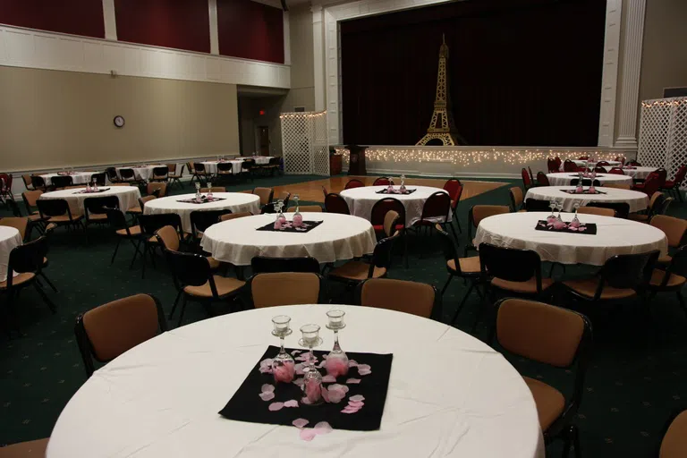 Centre Stage room set up for formal event. Round tables dressed with tablecloths and floral arrangements are throughout the room. Mini Eiffel tower with fairy lights on the stage. 