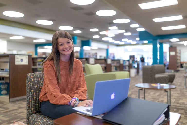 Student looks up from her laptop to smile at the camera