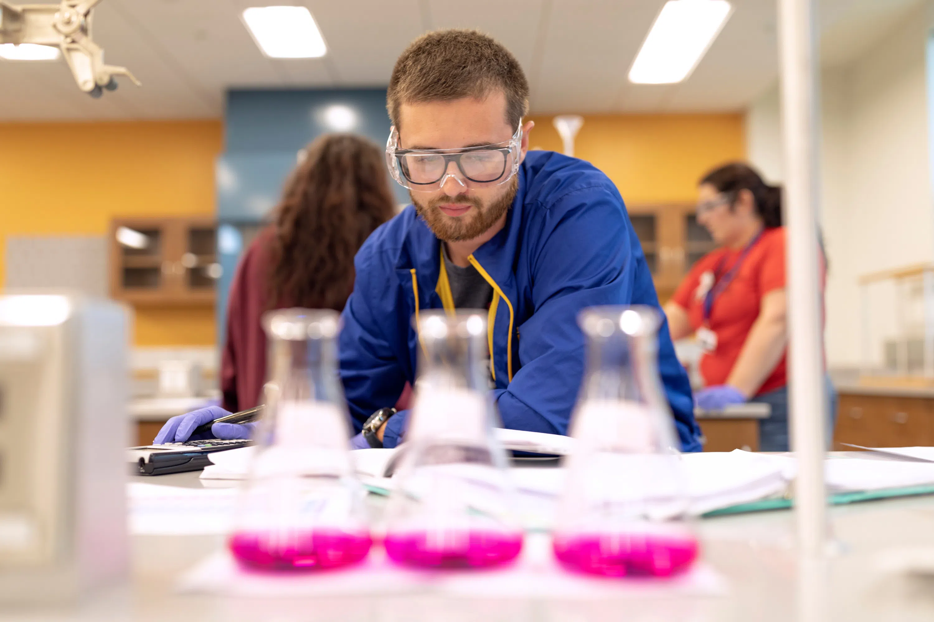 Student looks at three beakers with pink liquid in the Chemistry Lab