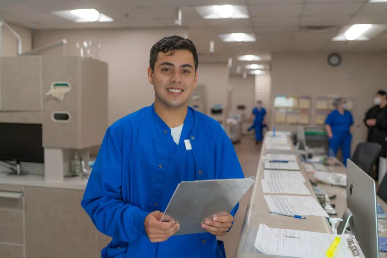 Student holding a clipboard smiles at the camera 