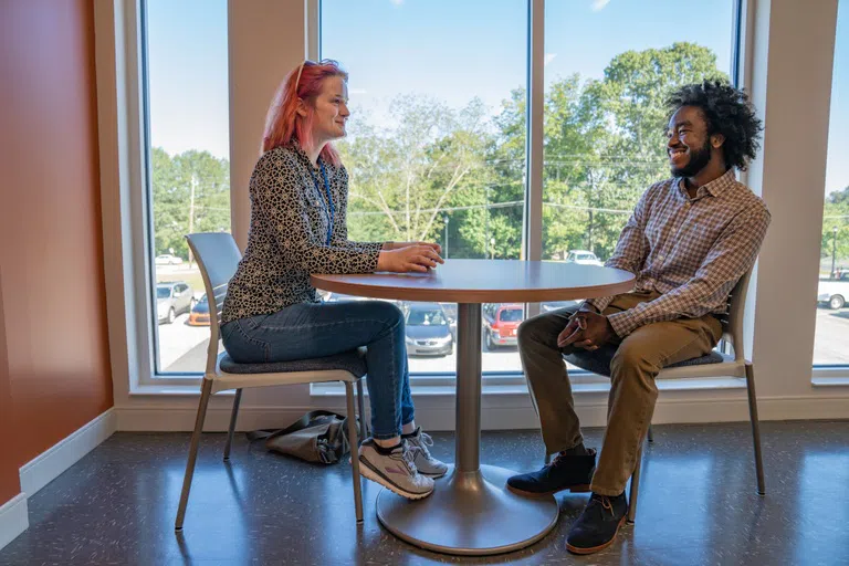 Two people sit at a table in front of a window