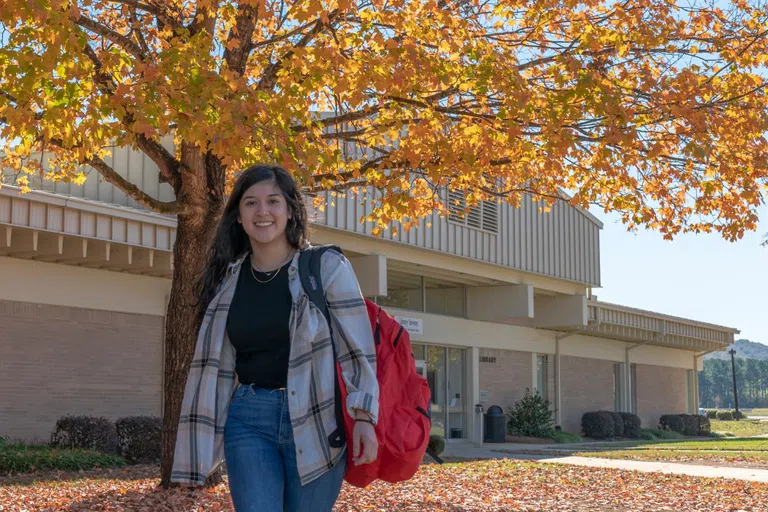 Female student stands in front of the library with her backpack