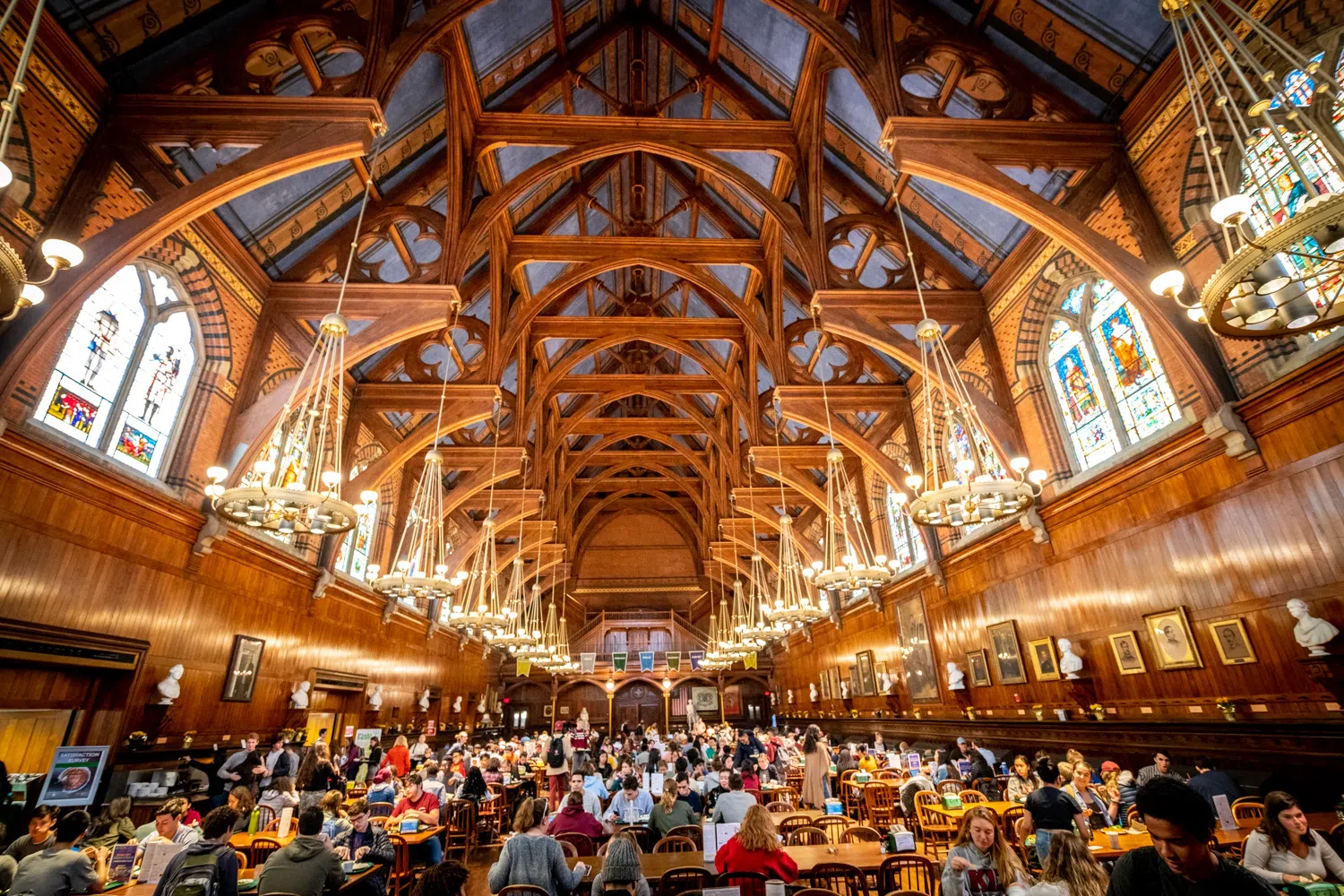 Students dine at tables in Annenberg Hall, with chandeliers and stained glassed windows.