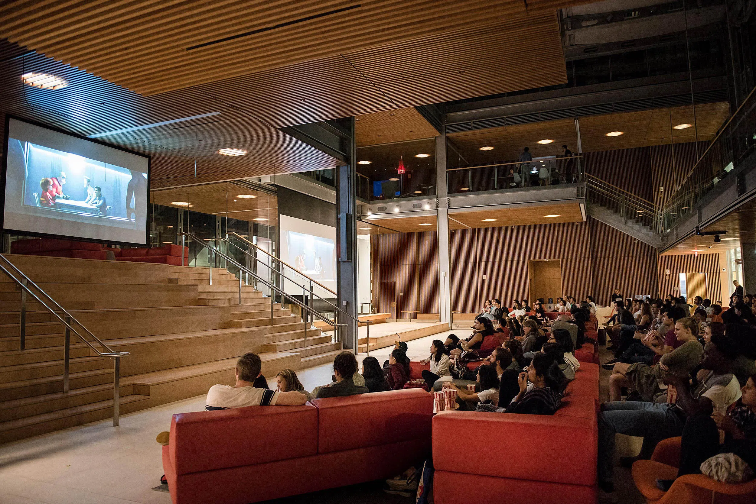 Students gather on couches, watching a projected movie in a large expansive room