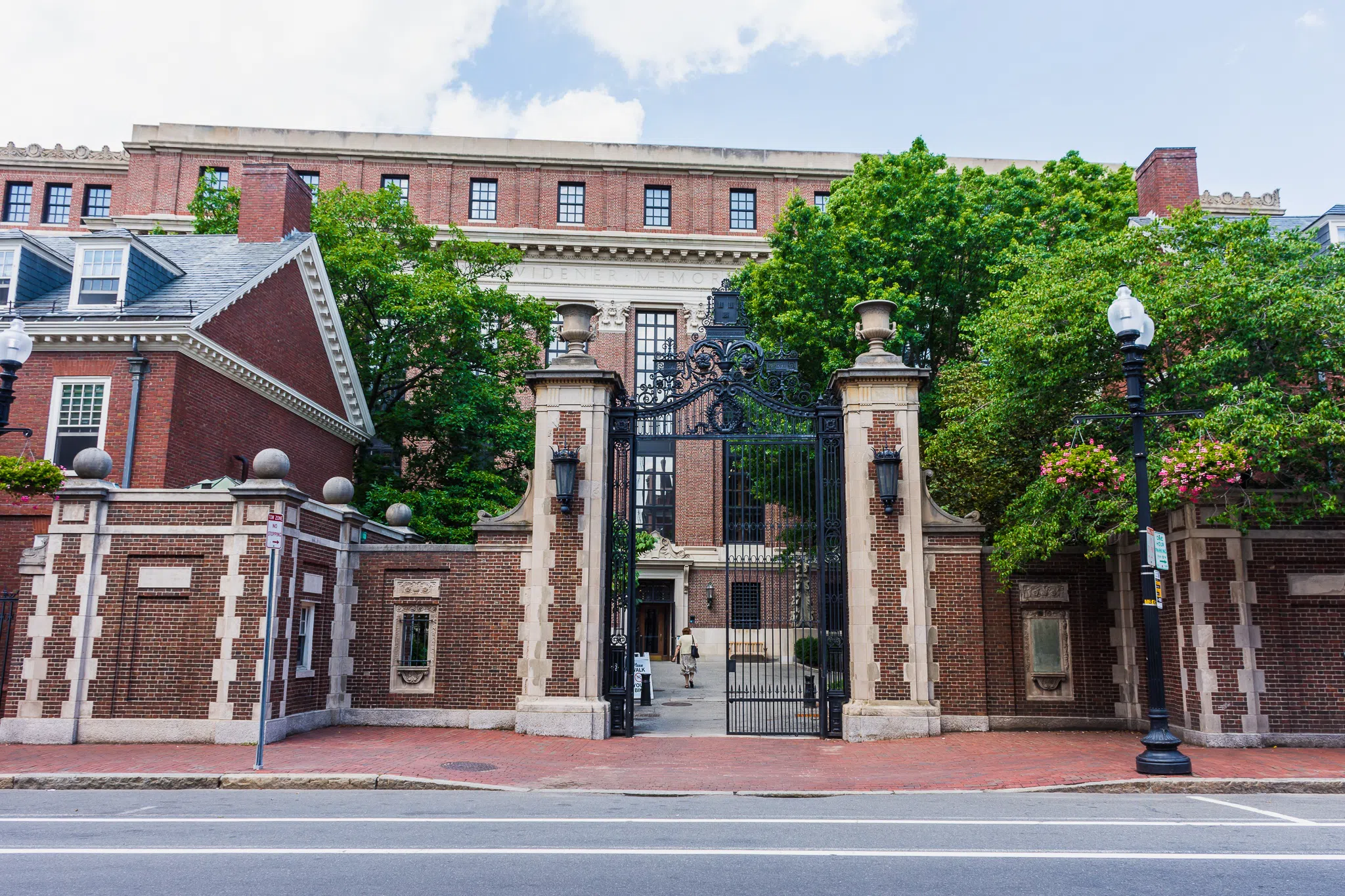 Red brick wall and iron gate gives entrance to Harvard Yard; large building inside gates