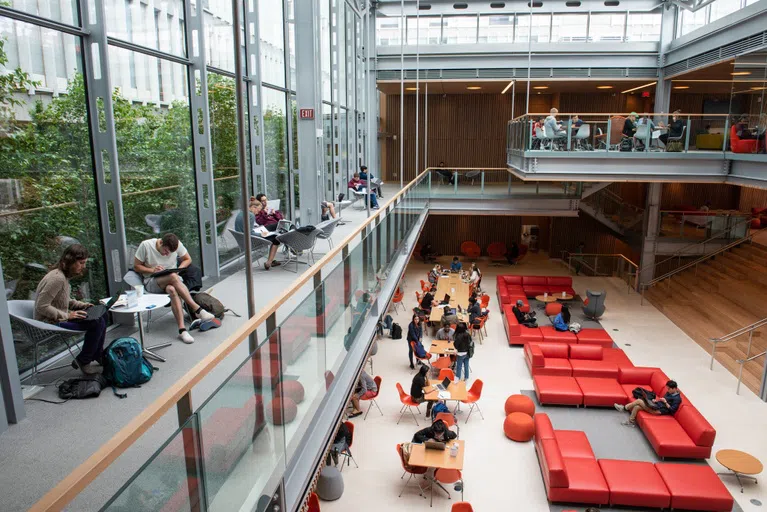 Glass-walled atrium with red couches and orange chairs; students studying