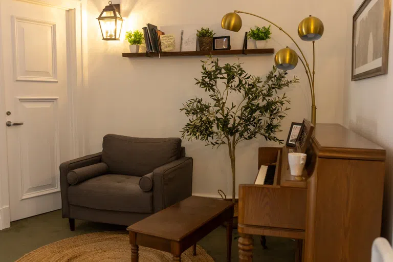 Piano and bench next to a grey love seat