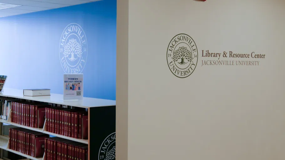 The entrance of the law library with the library logo on the wall. Behind the white wall is a blue-painted room with bookshelves of reference material.