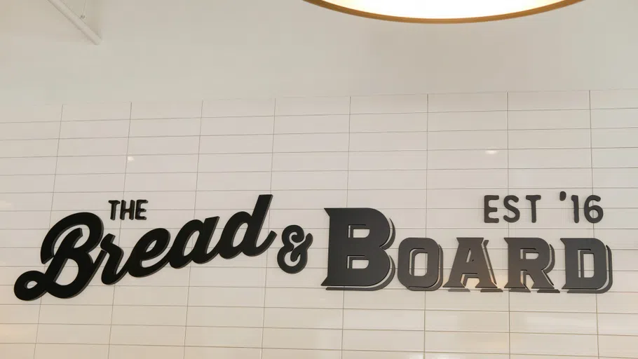 A white tile wall with the "Bread and Board" logo in black lettering over it.