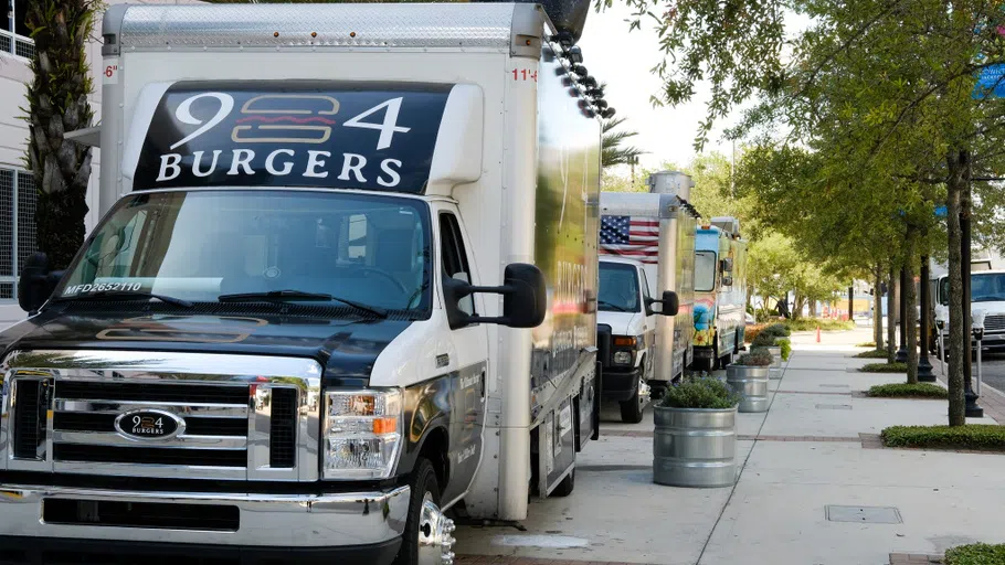 Four food trucks, lined up in front of a parking garage.