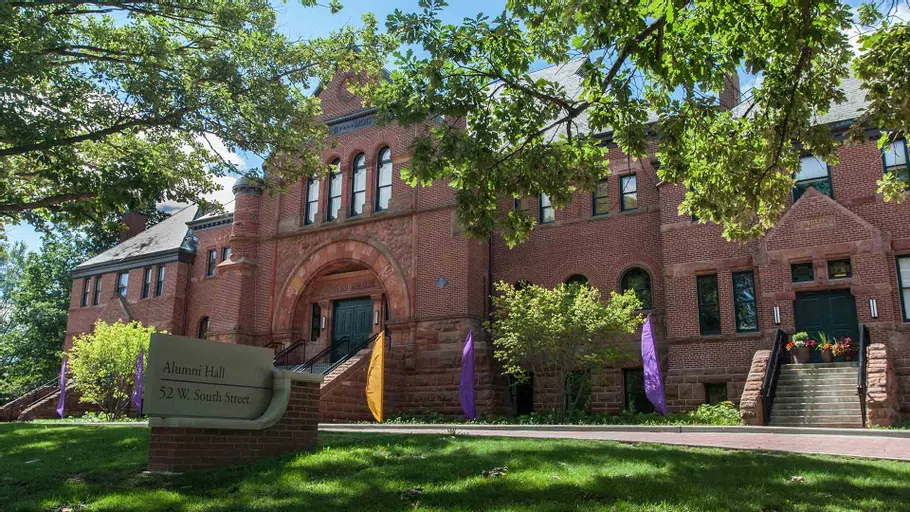 Purple and gold flags fly outside Alumni Hall on a summer day.