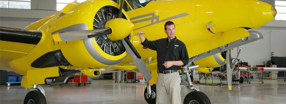 An instructor stands near airplane propeller. 