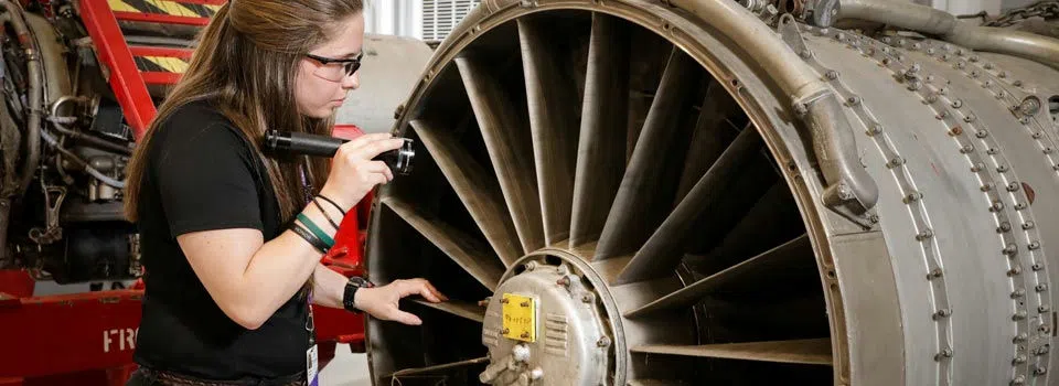 A student services an airplane engine.