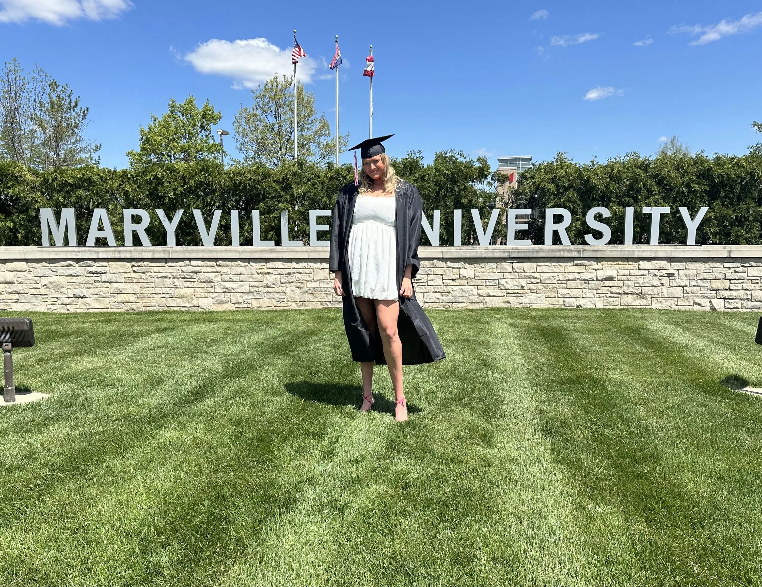 A student stands in the grass in front of the "Maryville University" sign.