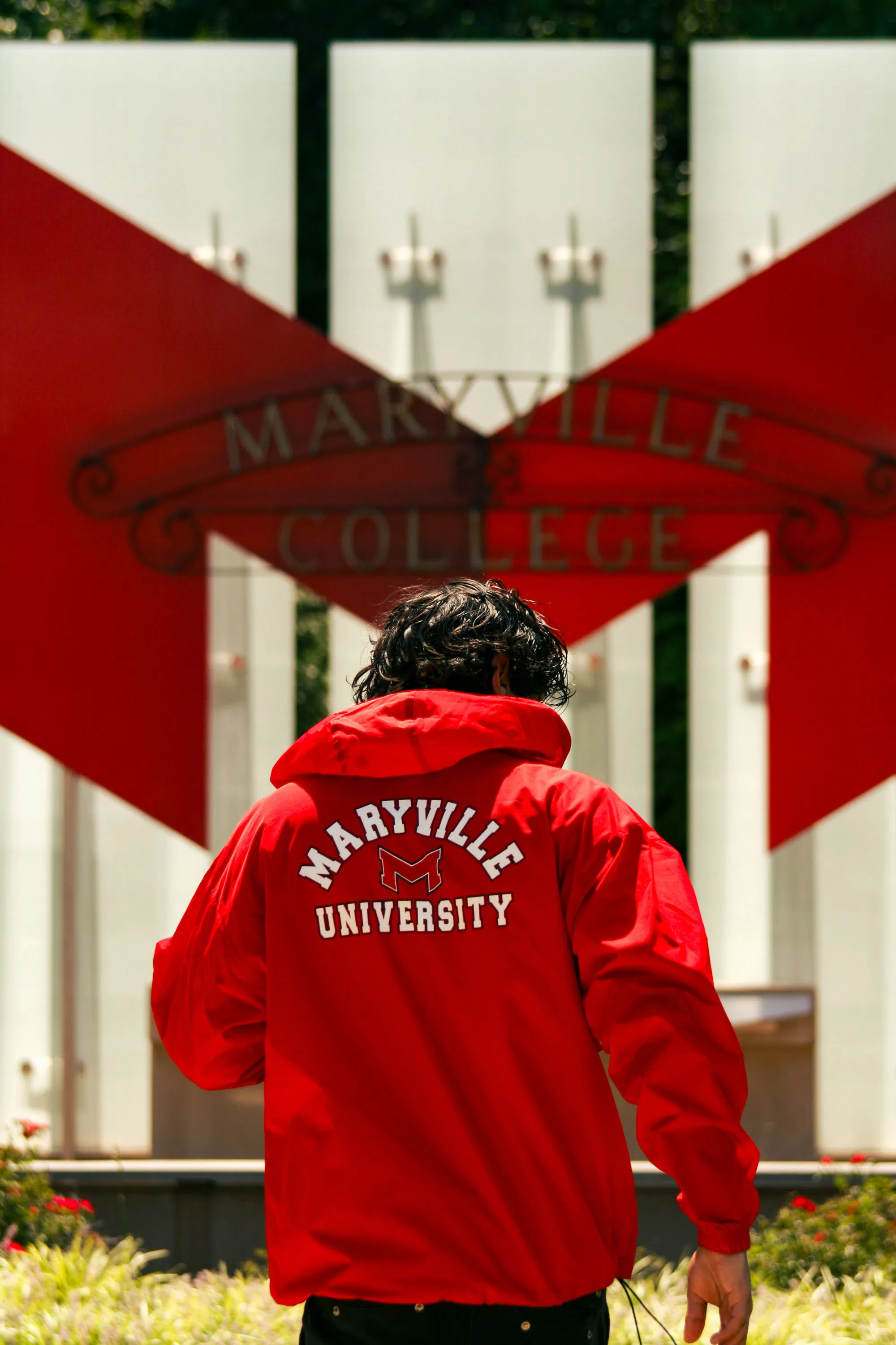 A student walks towards the Maryville sign wearing a red Maryville University pullover.