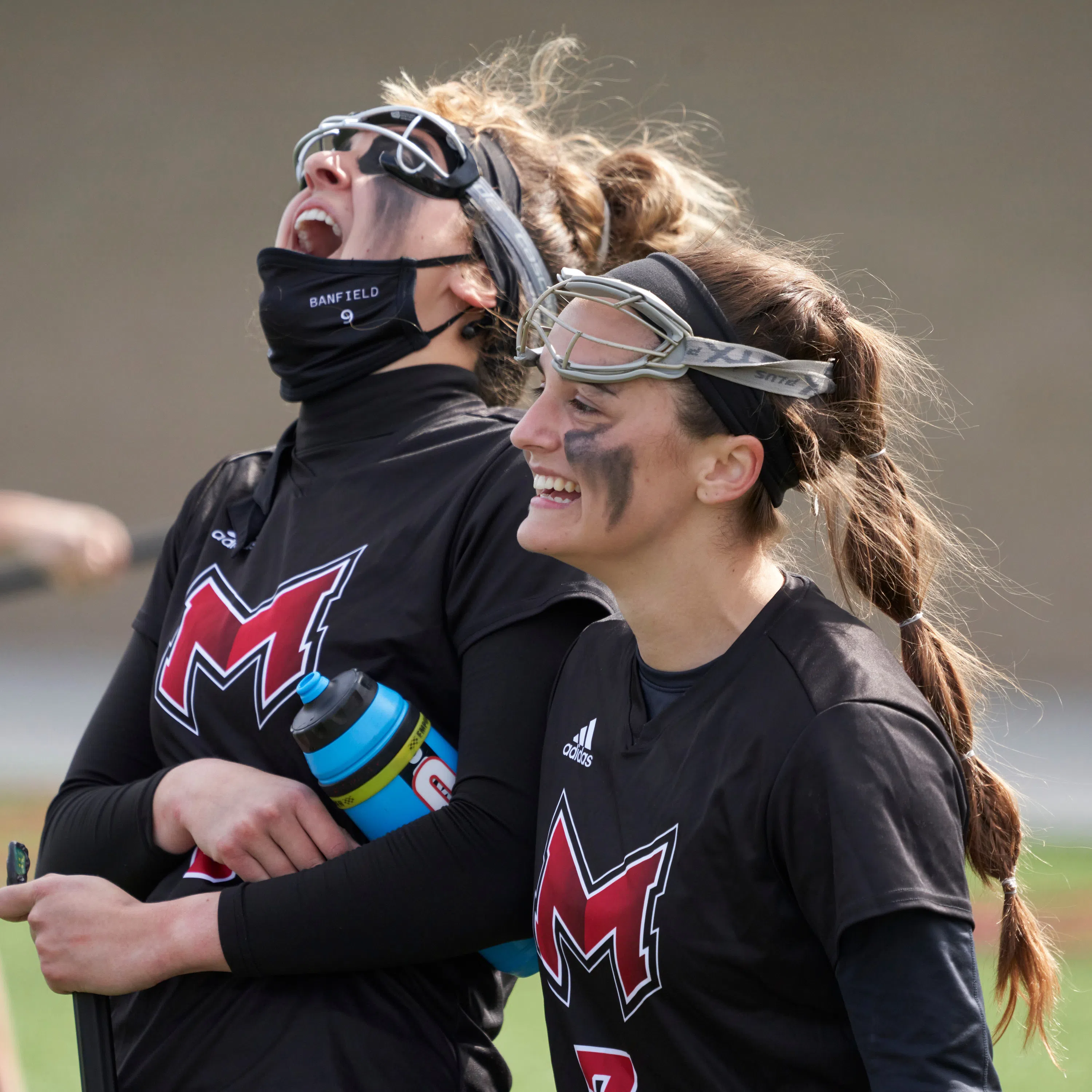 Teammates on the women's lacrosse team celebrate a goal on the sidelines.