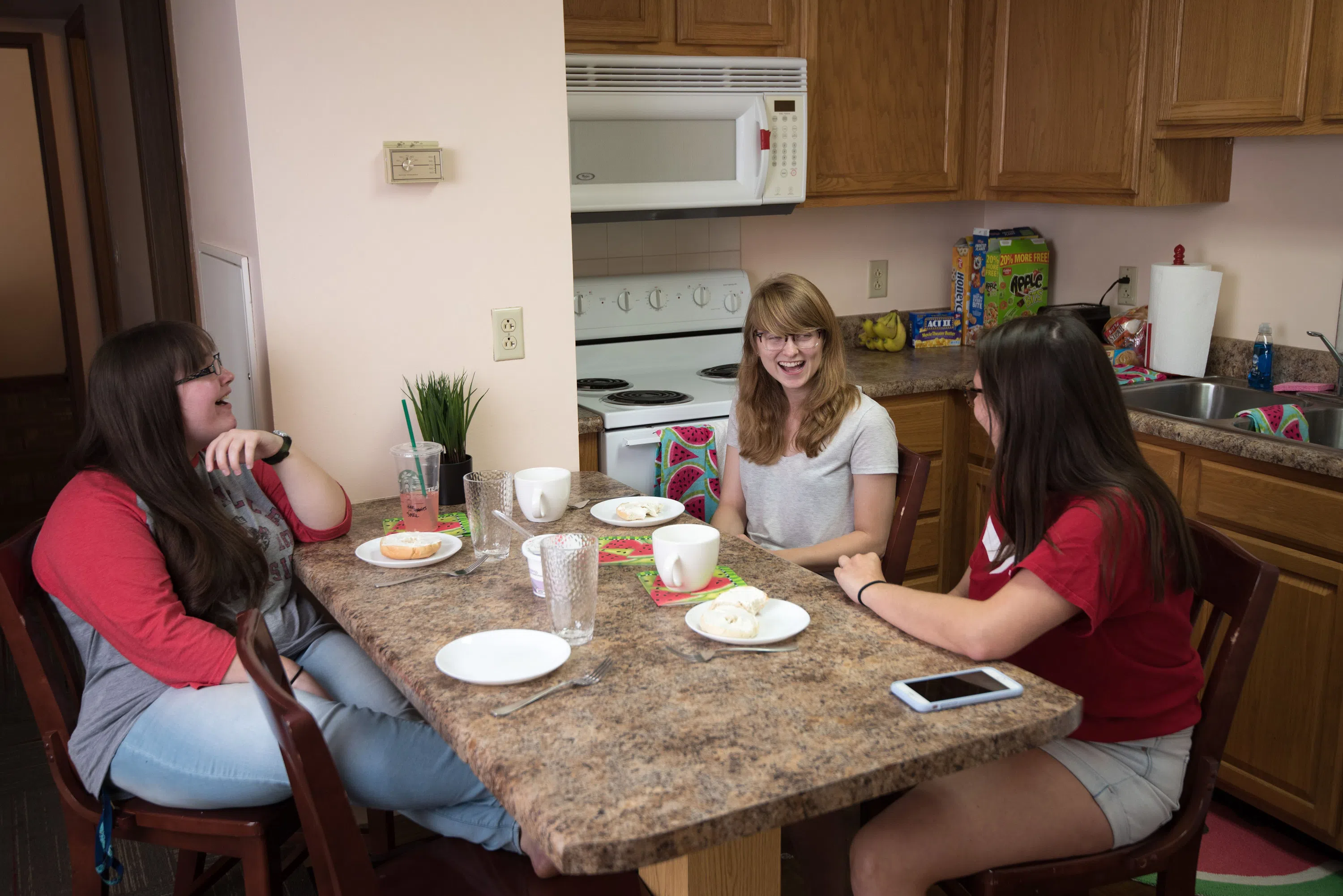 Students sit at the kitchen counter to grab a bite to eat. You can see the full kitchen in the background of the image.