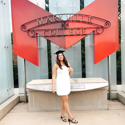 A student stands in front of a red "M" with the "Maryville College" sign