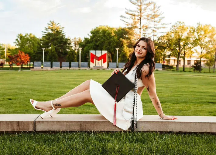 A student poses on the Maryville wall with the GAnder Quad and Maryville "M" in the background.