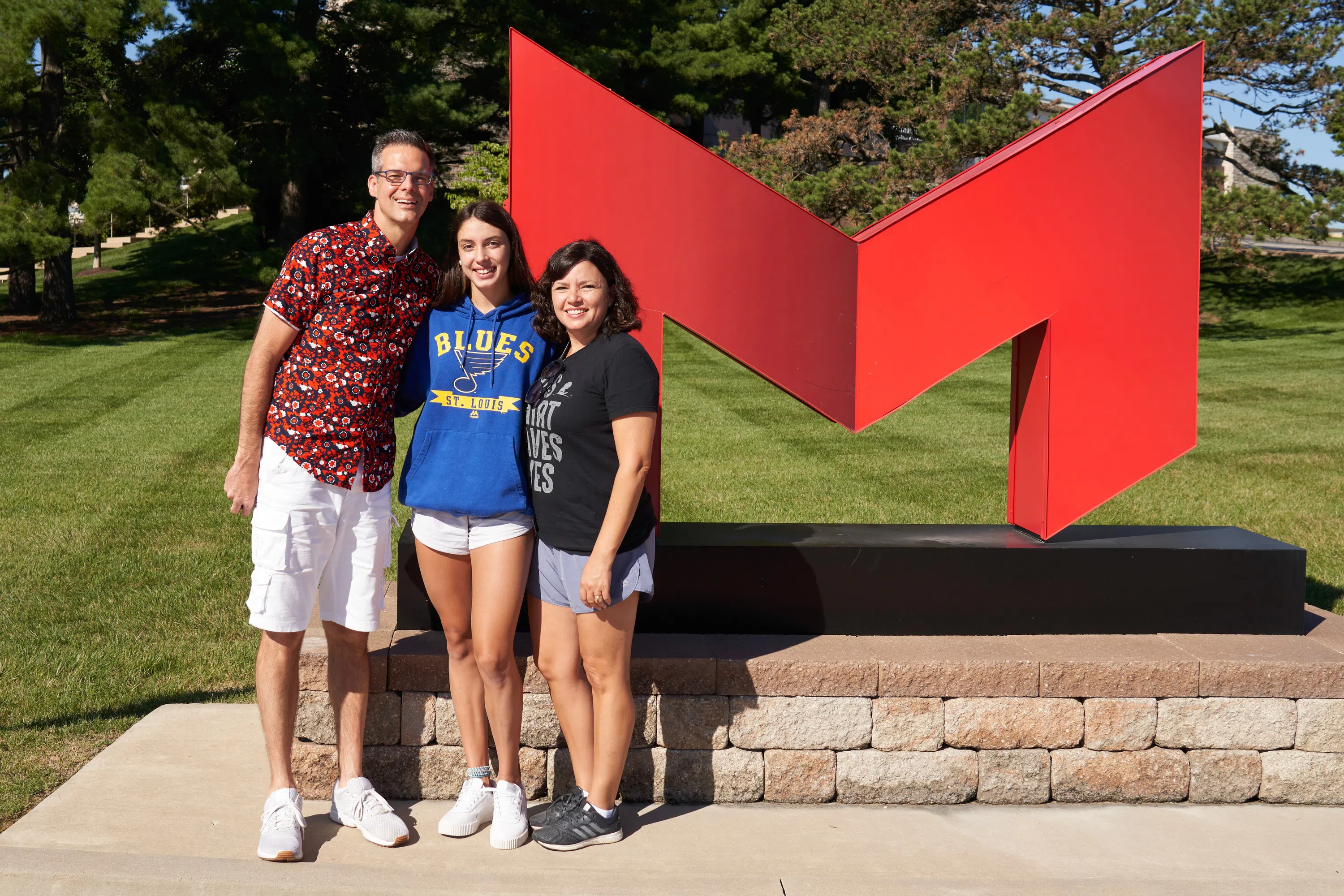 A family takes a photo at the "Big Red M" outside of Gander Hall.