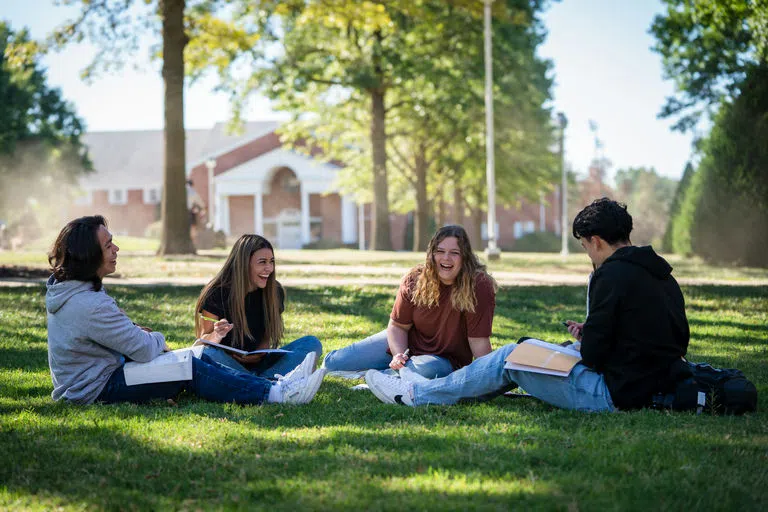 Four students sitting on the campus mall laughing