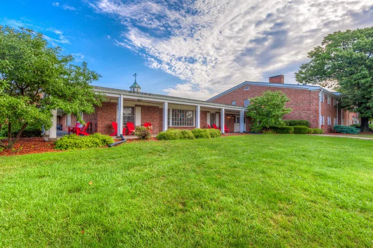 Exterior of community-style residence hall. Red lounge chairs sit on the exterior patio