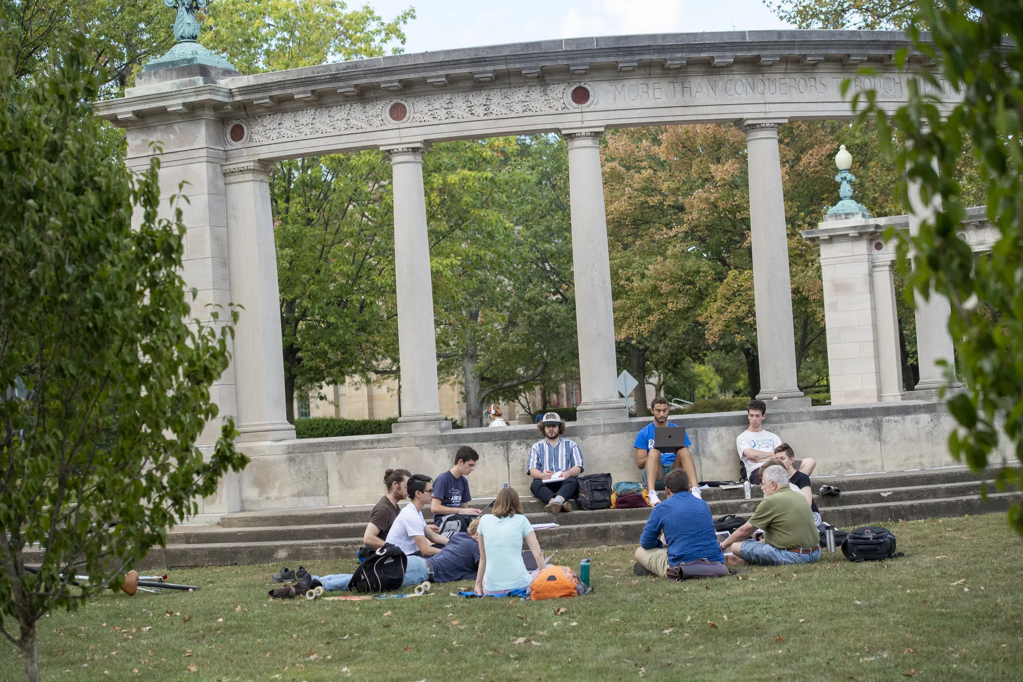 A group of students sit on the steps of the Tappan Square arch, a large semicircle sandstone structure.
