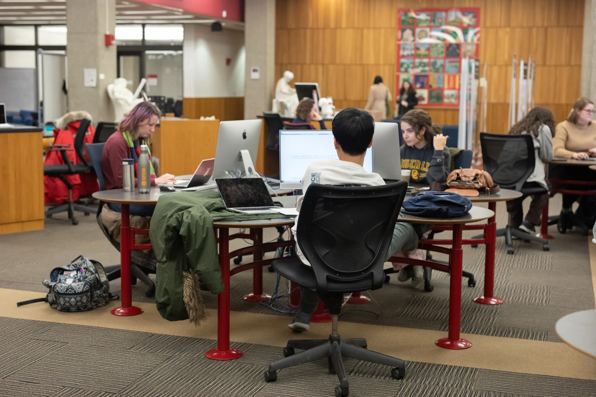 Three focused students sit in front of desktop computers working on assignments.