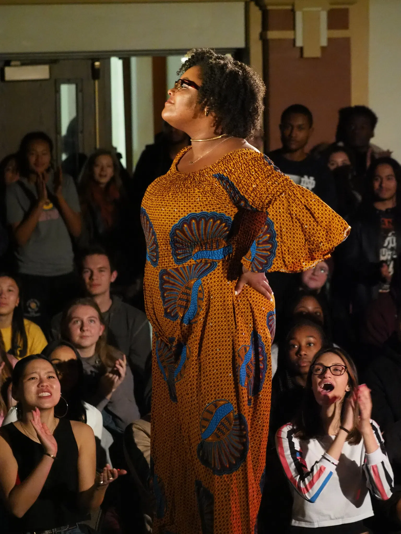 A Black student in a brightly colored dress poses at the end of the runway at Oberlin's annual Black history month fashion show.