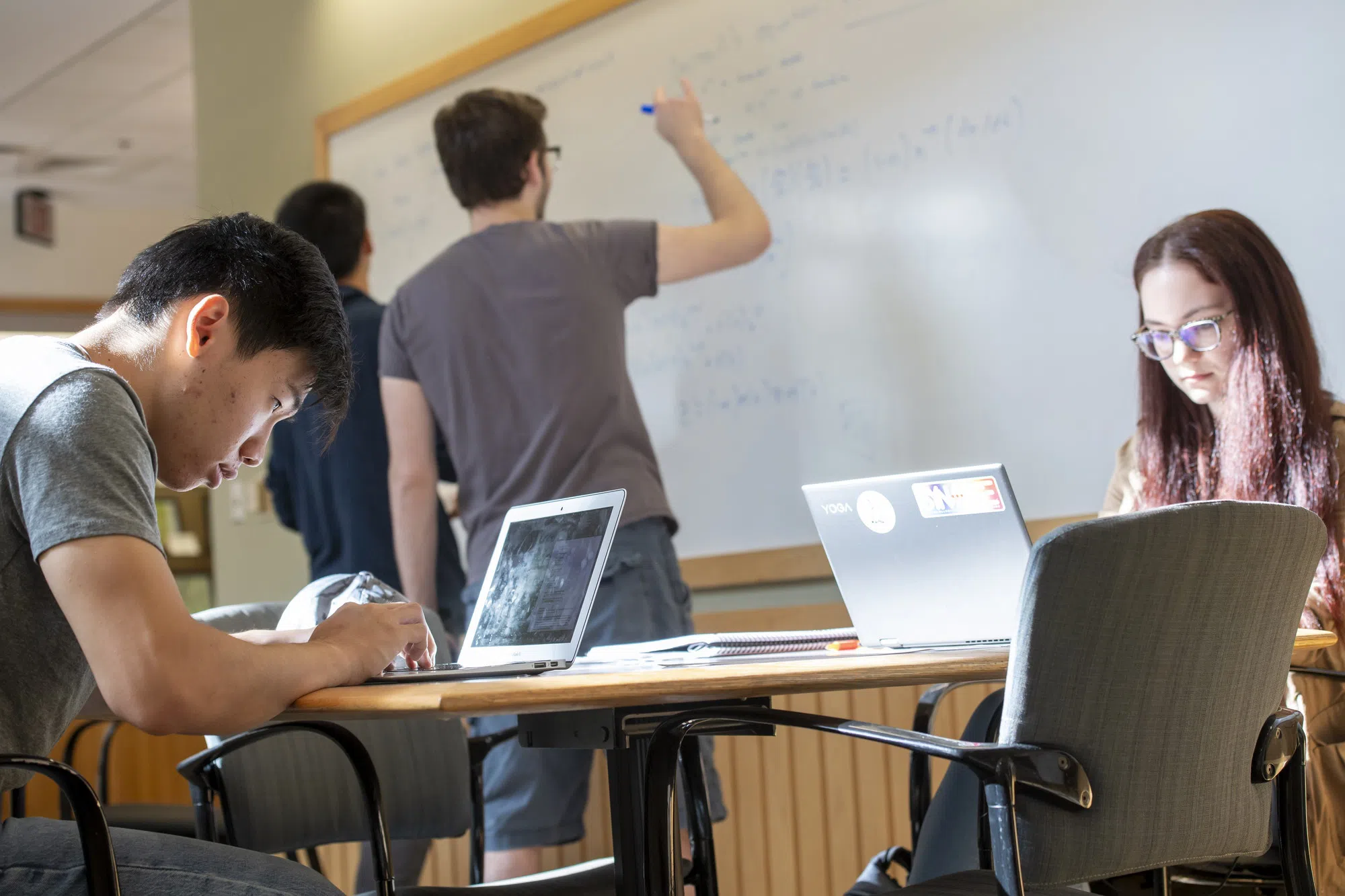 Students study on their computer and write on a whiteboard. 