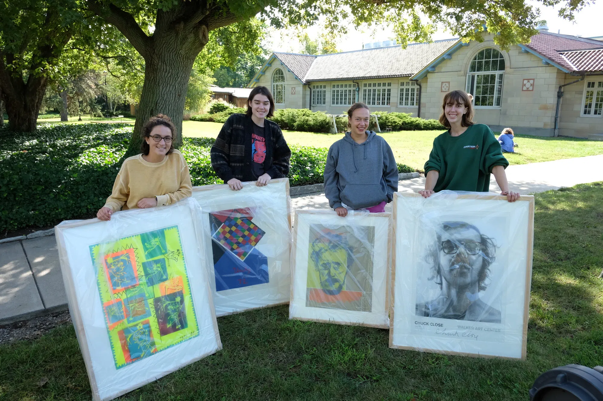 Four students are smiling as they hold large frames of artwork.