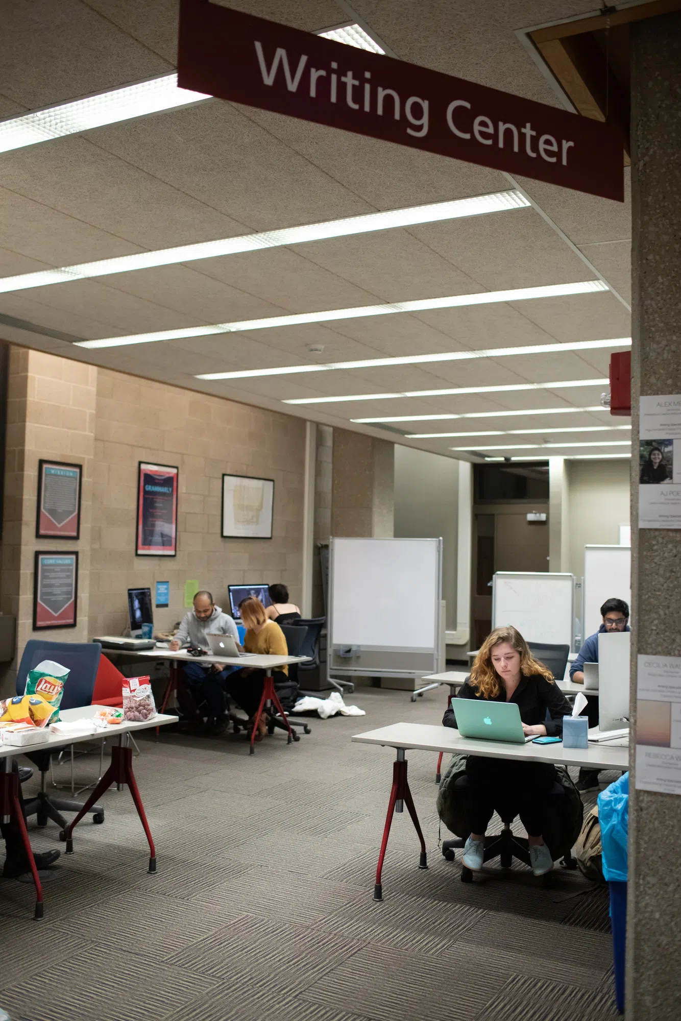 Students sit at desks in a big, well-lit room with whiteboards.