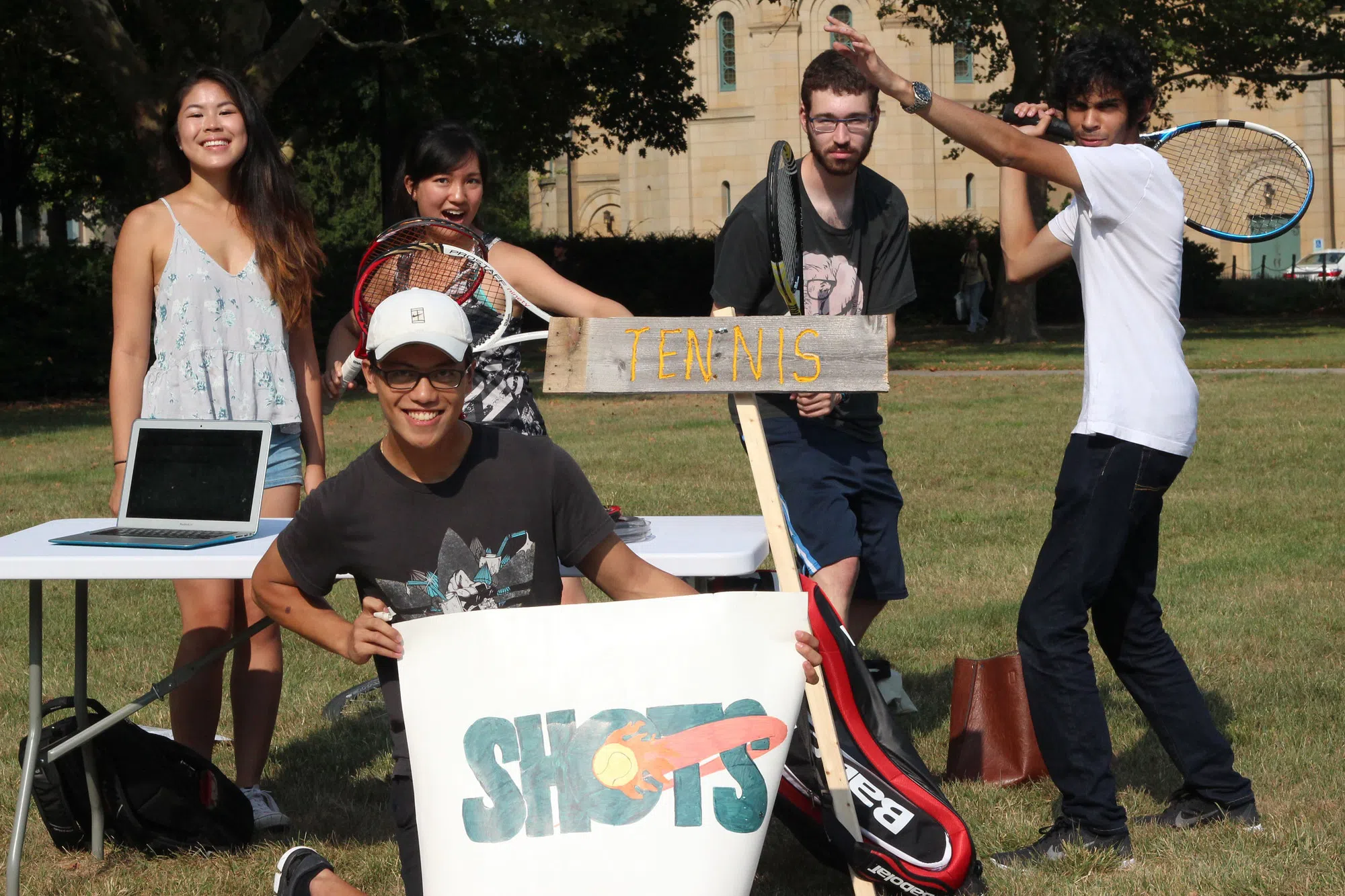 Five students hold tennis rackets and posters to promote the club table tennis team.