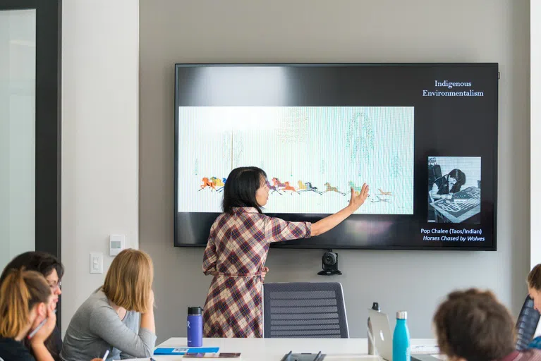 A presenter stands in front of a powerpoint that says Indigenous Environmentalism.