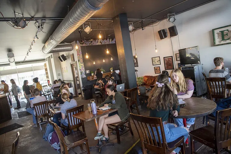 People sit at different tables in a dark wood, well-lit coffee shop.