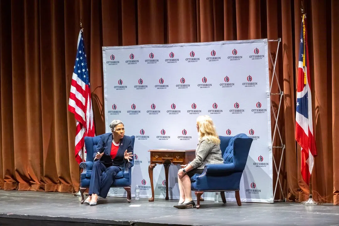 A lecture happening on stage. There are two women conversating with an Otterbein branded backdrop. The American flag and Ohio flag are on the left and right of them.