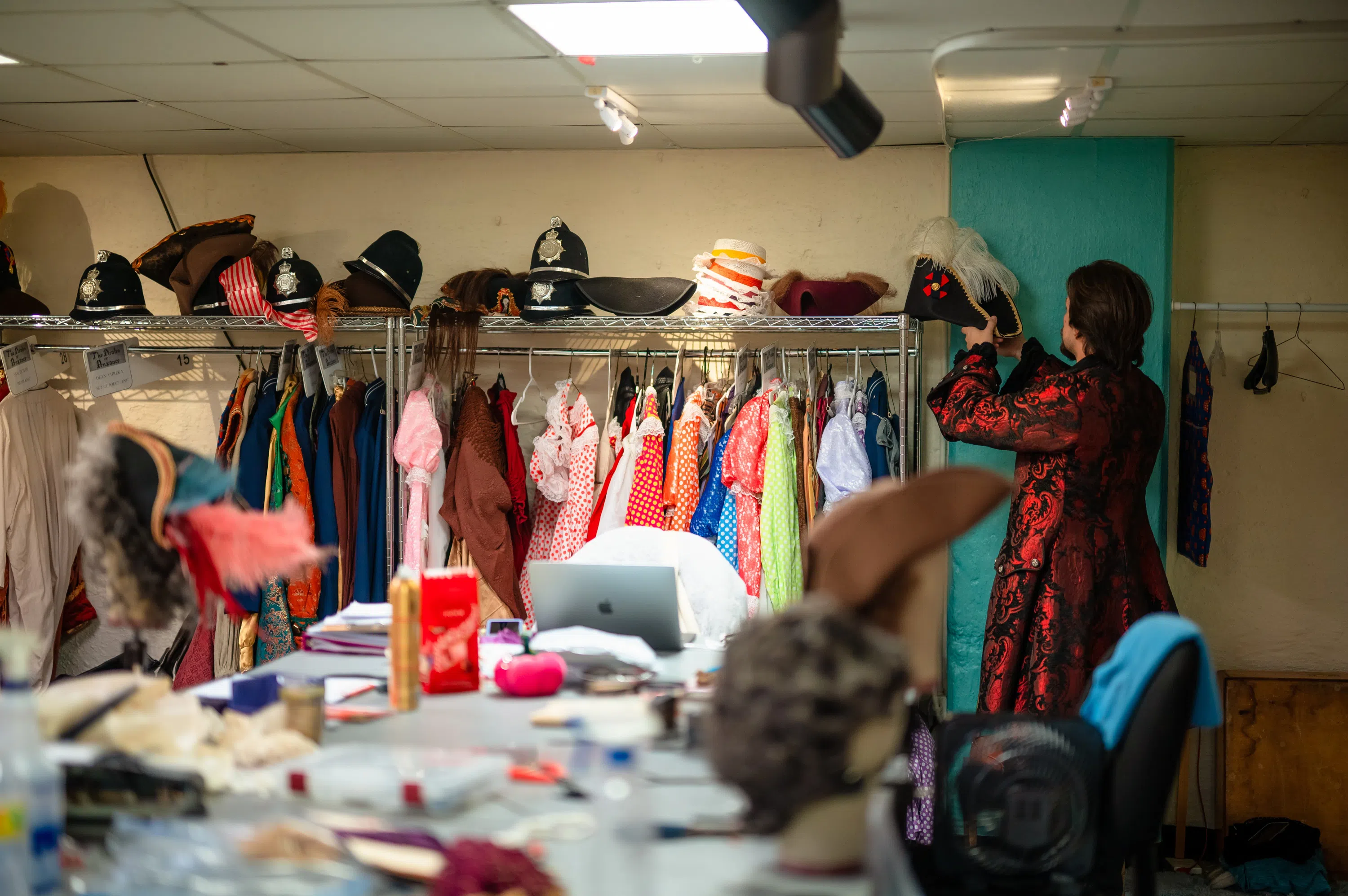 Costumes are hanging on a rack with a table full of various items.