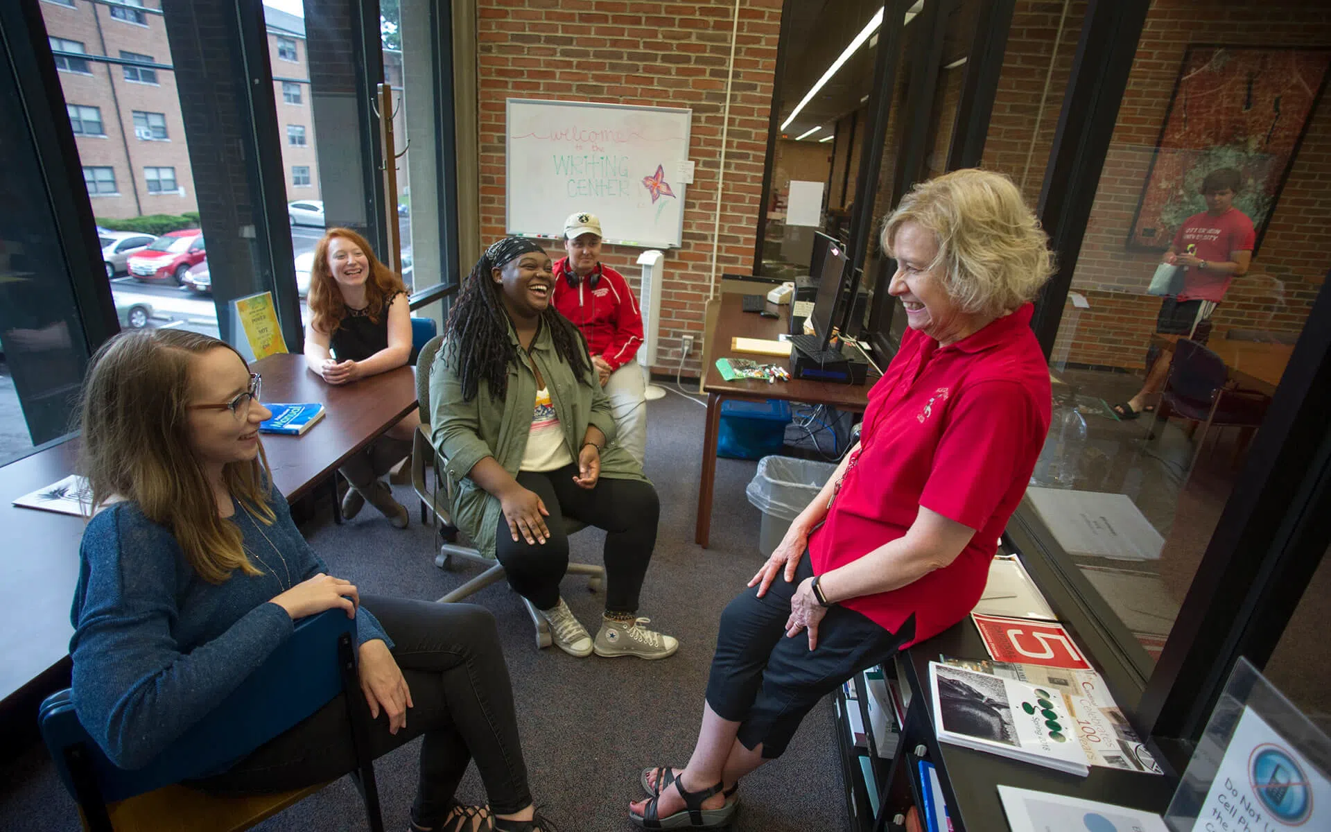 5 people gathered in a small classroom laughing with eachother.