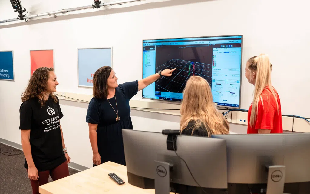 4 women in front of a large television screen observing a 3D chart.