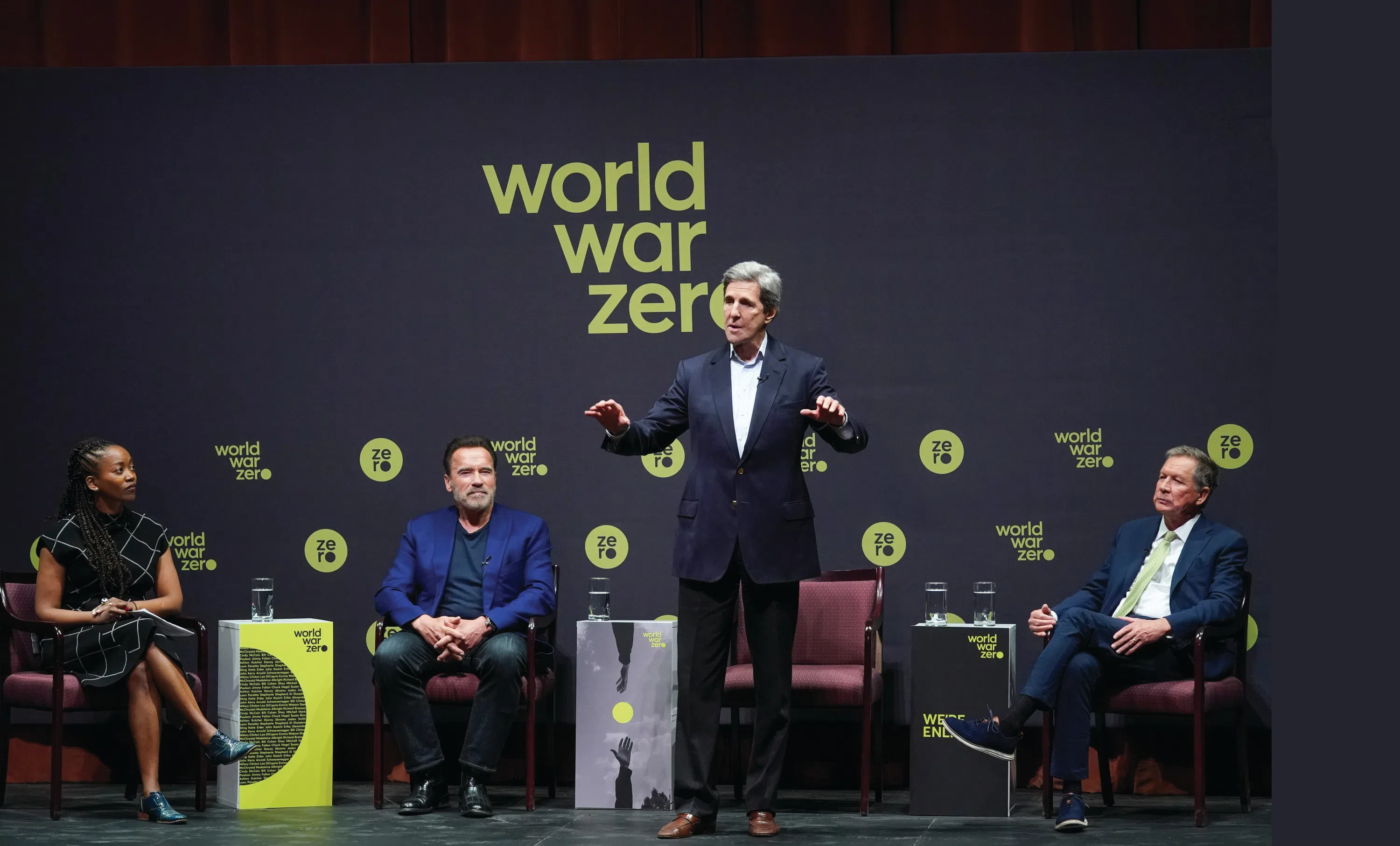 A group of people on stage at a lecture. The backdrop reads "world war zero"