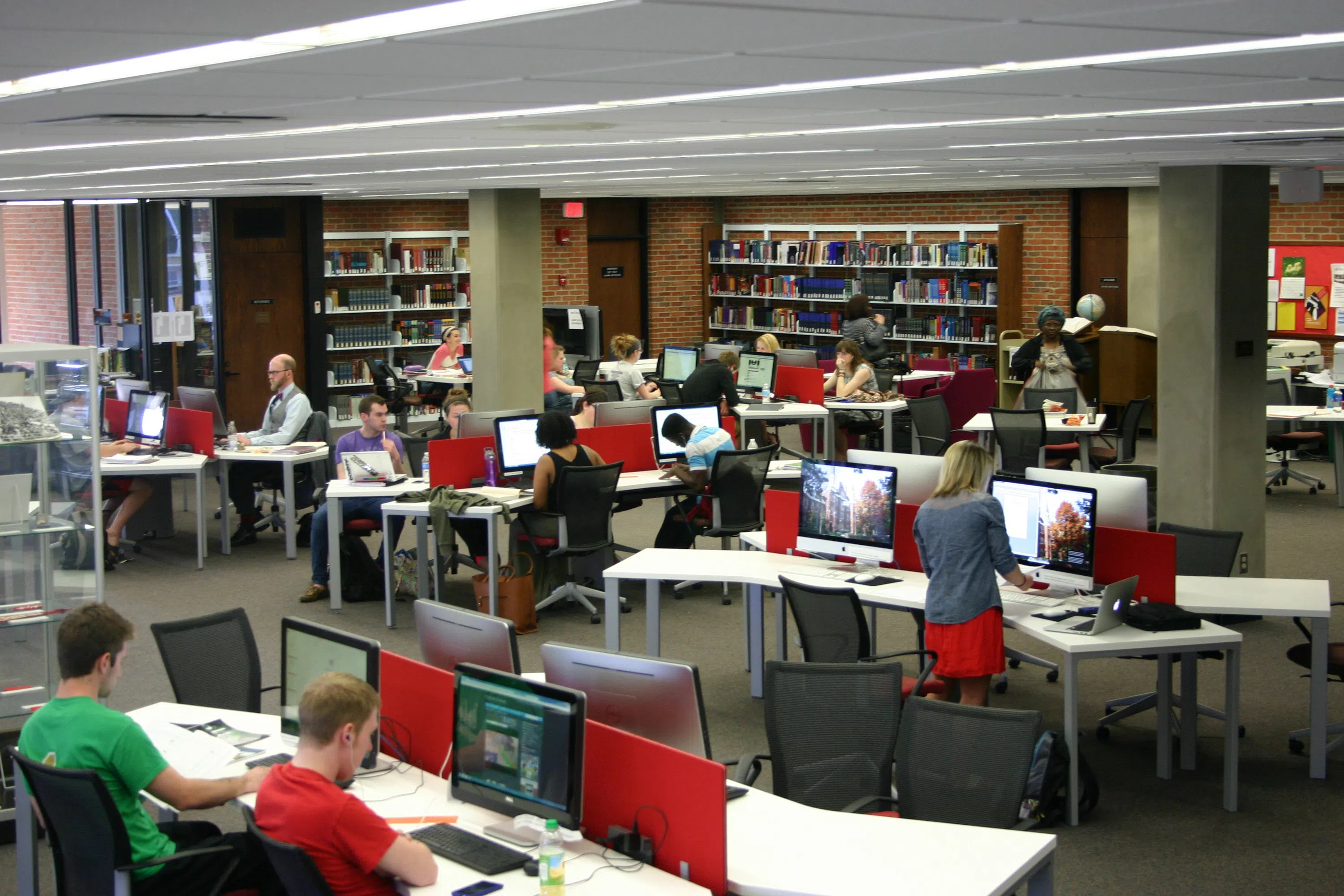Lively view of the main floor of the Library, tables for groups, public computers, and library staff all in one convenient area.