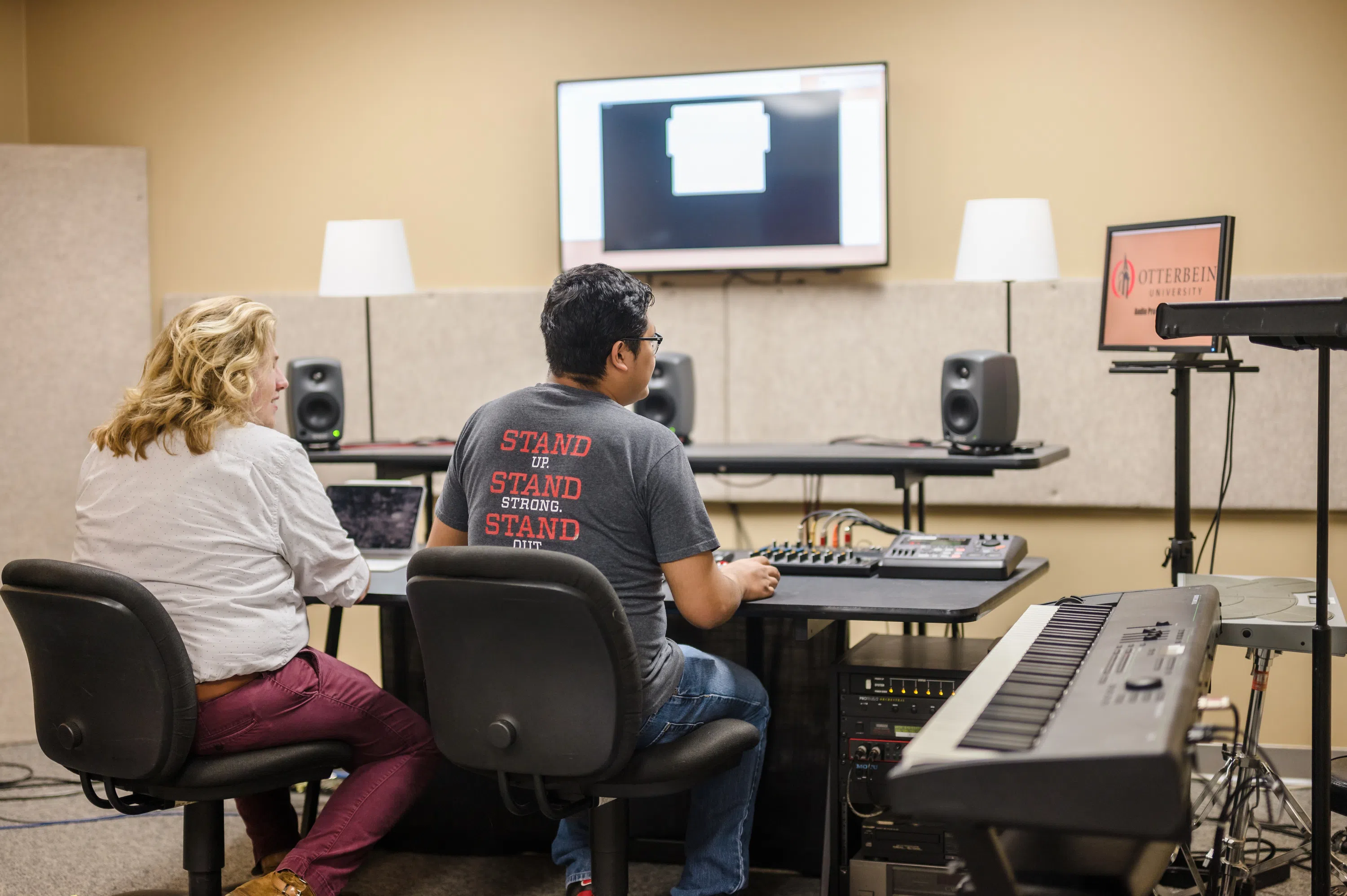 Two people sit in the music studio doing work